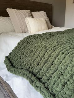 a large green blanket on top of a bed next to two pillows and a pillow case