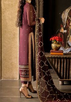 Introducing our Winter collection 'VELVET FESTIVE' by Asim Jofa designed to make you look and feel your best these pieces will add a touch of class and elegance to your wardrobe. Step into the embrace of timeless maroon, where elegance is not just a choice, but an effortless exhalation. This ensemble is a celestial canvas adorned with a constellation of 9mm gold sequins, twinkle-sized 3mm antique gold sequins, and a harmonious blend of matching zariwork and lurex, together weaving a tapestry of pure enchantment. The long shirt is a saga of opulence, embroidered from the neckline down to the very hem, an echo of grandeur that dances in harmony with the matching dupatta. The velvet-clad daman border is like a sentinel of sophistication. This is more than just an outfit, it's a time-honored t Pakistani Designer Clothes, Asim Jofa, Deep Maroon, Readymade Saree, The Embrace, Suit Fabric, Silk Dupatta, Gold Sequins, Model Pictures