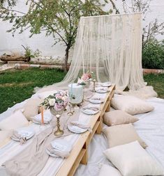 a table set up with white linens and place settings for an outdoor dinner party