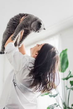 a woman holding a cat up in the air with her head above her head and eyes closed