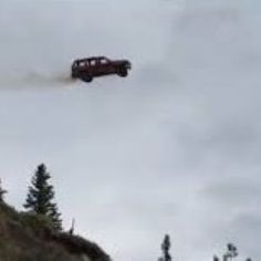 a red truck flying through the air over a hill with trees on both sides and an airplane in the sky above