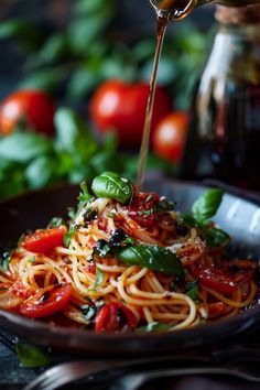 someone is pouring sauce over a plate of spaghetti with tomatoes and basil on the side