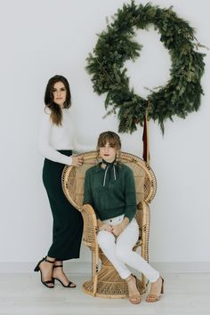 two women sitting on wicker chairs in front of a christmas wreath and a green wreath