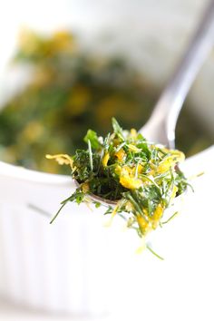 a white bowl filled with green and yellow food next to a spoon on top of a table