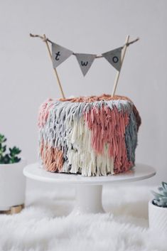 a cake decorated with fringes and bunting on top of a white table next to potted plants