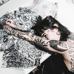 a tattooed woman laying on the floor next to some drawings