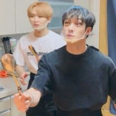 two young men standing in a kitchen with spoons and utensils on the counter