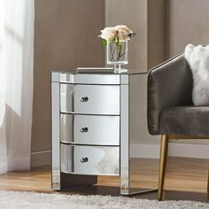 a mirrored side table with three drawers and a flower in a vase on the top