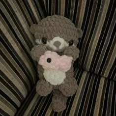 a stuffed animal is sitting on a striped couch with a pink flower in it's mouth