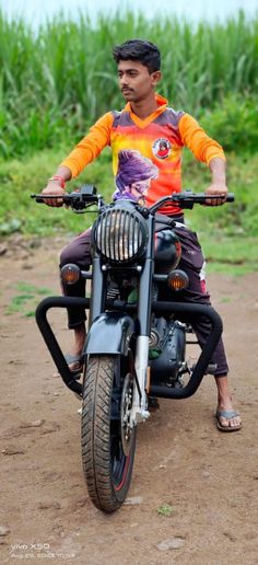 a man riding on the back of a motorcycle down a dirt road in front of a corn field