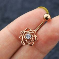 a gold nose ring with a flower design and a diamond in the center, on a person's finger