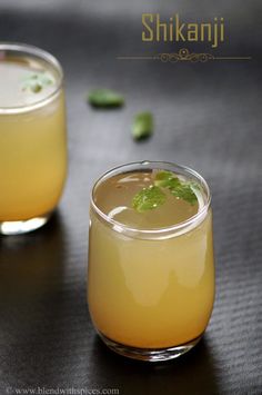 two glasses filled with drinks sitting next to each other on a black tableclothed surface