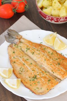 two fish fillets on a white plate with lemons and tomatoes