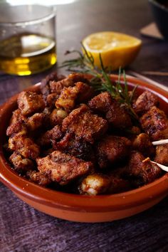 a bowl filled with meat sitting on top of a table next to lemon wedges