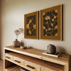 two paintings hanging on the wall above a wooden table with drawers and baskets underneath them