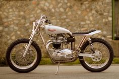 a motorcycle is parked on the street next to a stone wall and green grass in front of it