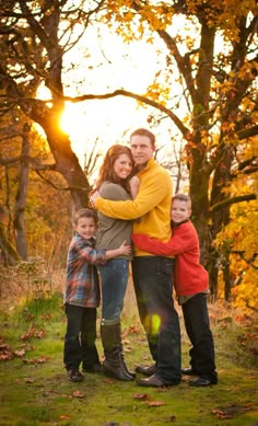 a family posing for a photo in front of some trees with fall leaves on the ground