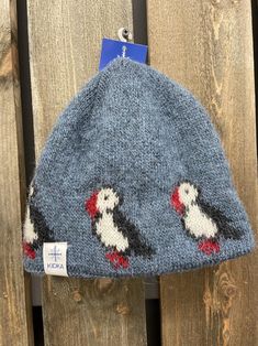 a knitted hat with two penguins on it hanging from a wooden fence next to a sign