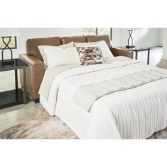 a bed with white comforter and pillows in a room next to a brown chair