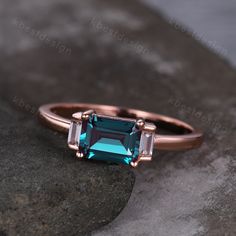 a ring with an emerald colored stone in the middle and two baguettes on each side