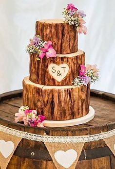 a wedding cake is sitting on top of a barrel with pink flowers and greenery