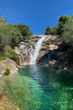 there is a small waterfall in the middle of this lake with clear blue water and green vegetation