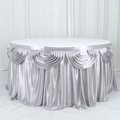 a round table covered in silver cloth with pleated drapes on the top and bottom