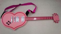 a pink guitar shaped like a heart with buttons and keys attached to the neck strap