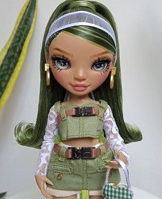 a doll with green hair is standing on a white surface next to a potted plant