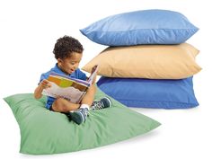 a young boy sitting on a bean bag reading a book with three pillows behind him