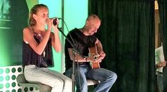 a man and woman singing into microphones while playing guitar in front of an audience