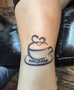 a woman's foot with a tattoo on it that reads mom and has a coffee cup in the shape of a heart