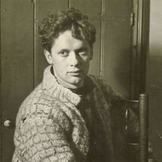 a black and white photo of a man sitting in front of a door wearing a sweater