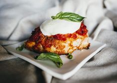 a white plate topped with lasagna covered in sauce and greens on top of a blanket