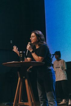 a woman standing in front of a microphone on top of a wooden table next to a man