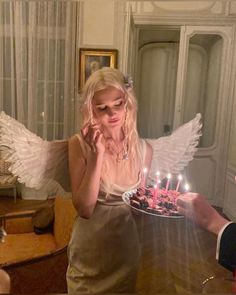 a woman holding a cake with candles in her hands and an angel wing on top