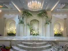 a large room with stairs and chandelier in the center, surrounded by greenery