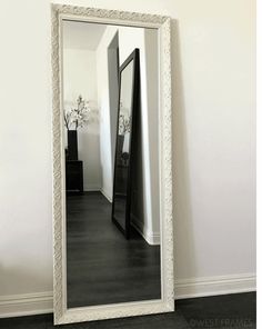 a large mirror sitting on top of a wooden floor next to a white wall with a vase in it