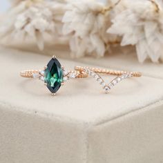 two rings with green and white stones in them on a table next to some flowers