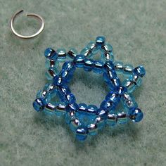 a blue beaded star ornament sitting on top of a gray surface next to a silver ring