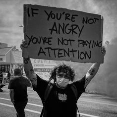 a man holding up a sign that says if you're not angry you're not paying attention