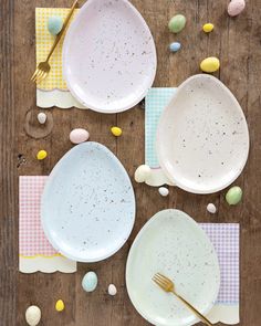 three plates and two forks on a wooden table with easter eggs scattered around them in the background