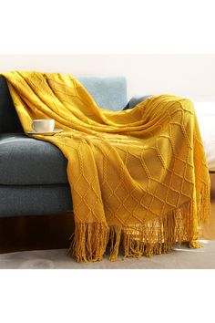 a couch with a yellow blanket on top of it next to a cup and saucer