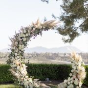 a wedding arch with flowers and greenery on the ground in front of a hedge