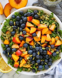 a white bowl filled with blueberries, peaches and pistachio on top of a marble counter