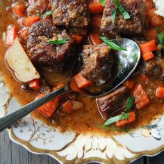 a bowl filled with stew and carrots on top of a wooden table next to a spoon