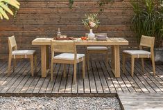 a table and chairs on a wooden deck in front of a wood fence with potted plants