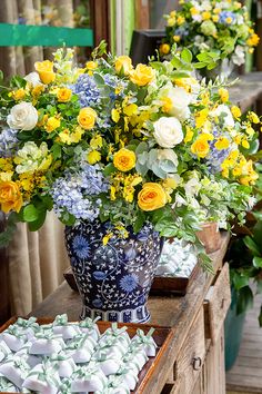 a blue vase filled with yellow and white flowers on top of a table next to plates