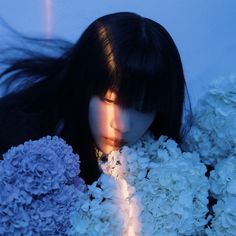 a woman with long black hair is surrounded by white flowers