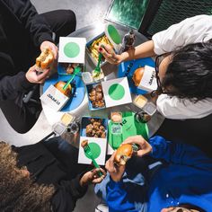 several people sitting around a table with food and drinks in their hands, looking down on them